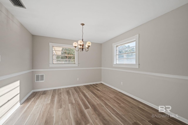 empty room with hardwood / wood-style floors and a notable chandelier