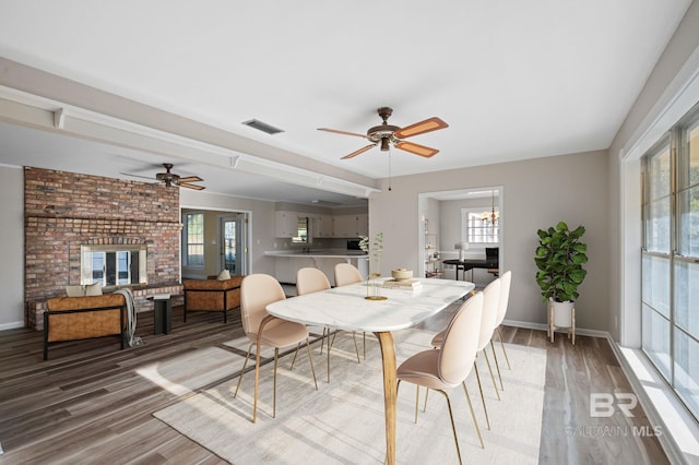 dining area with hardwood / wood-style flooring, ceiling fan, and a brick fireplace