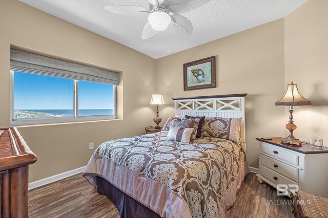 bedroom with dark wood-type flooring, a water view, a textured ceiling, and ceiling fan