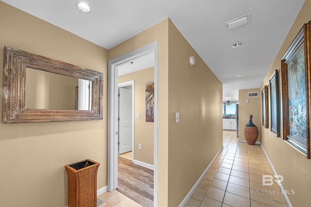 hallway with a textured ceiling and light tile patterned floors