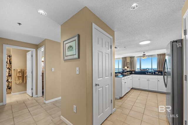 kitchen with a textured ceiling, stainless steel refrigerator, light tile patterned floors, and white cabinets