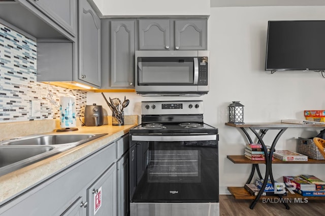 kitchen with dark wood-type flooring, stainless steel appliances, decorative backsplash, and gray cabinets