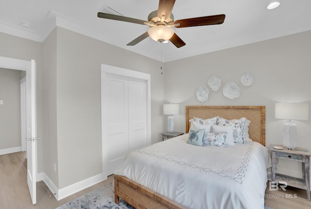 bedroom featuring ornamental molding, a closet, light wood-style floors, baseboards, and ceiling fan