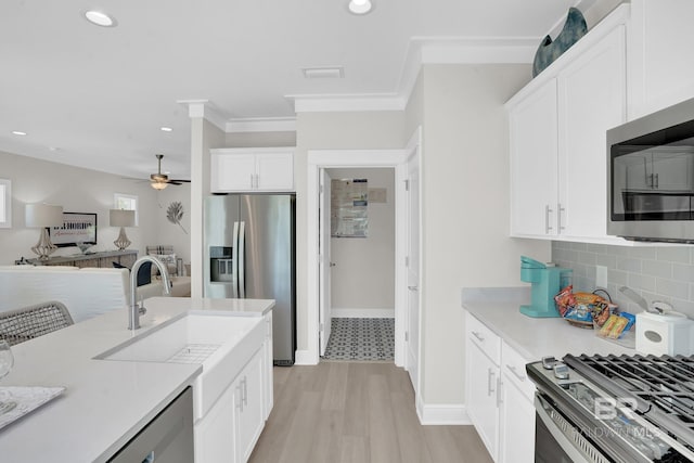 kitchen featuring crown molding, light countertops, appliances with stainless steel finishes, white cabinets, and a sink