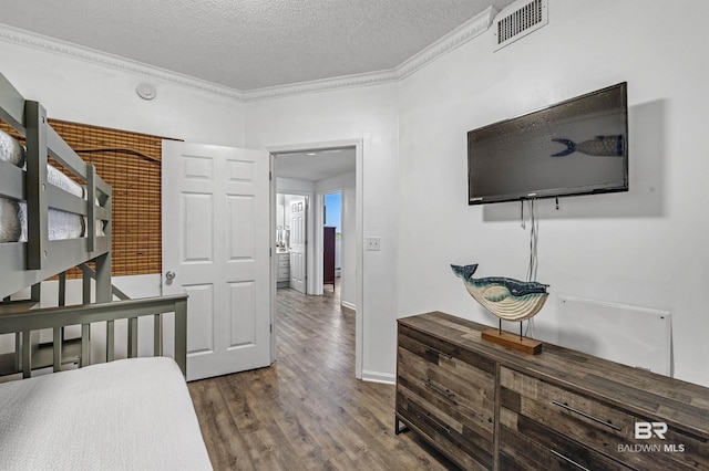 bedroom featuring visible vents, ornamental molding, a textured ceiling, wood finished floors, and baseboards