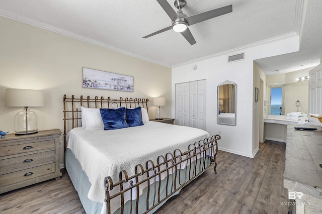 bedroom featuring a closet, visible vents, ornamental molding, a textured ceiling, and wood finished floors