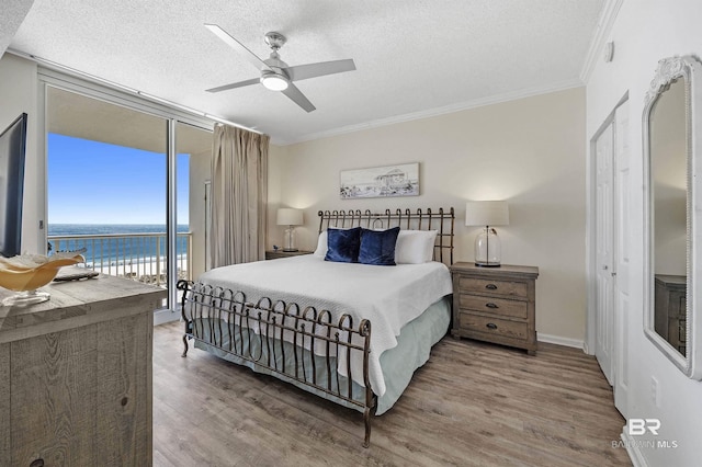 bedroom featuring a textured ceiling, wood finished floors, access to outside, ornamental molding, and expansive windows