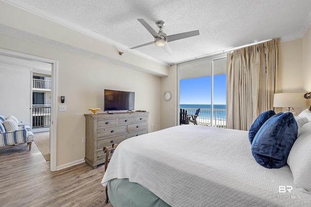 bedroom with wood finished floors, access to exterior, a wall of windows, crown molding, and a textured ceiling