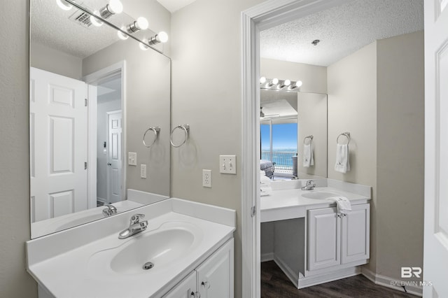 bathroom featuring two vanities, a sink, a textured ceiling, and wood finished floors