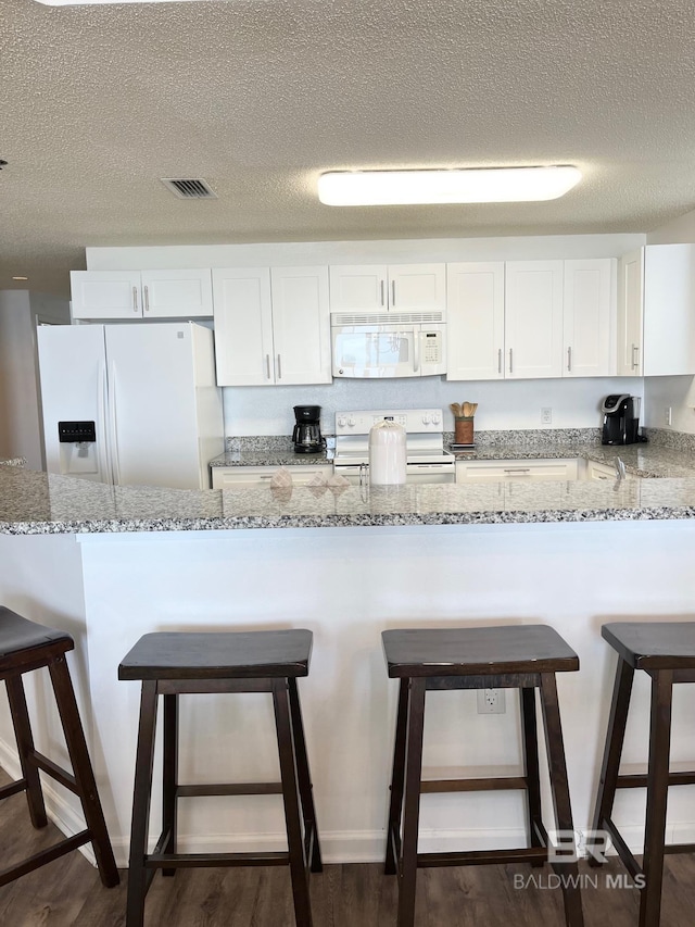 kitchen featuring white appliances, visible vents, a breakfast bar area, and white cabinets