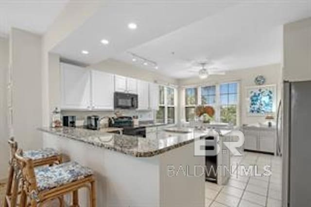 kitchen with light tile flooring, stainless steel refrigerator, white cabinets, kitchen peninsula, and stove