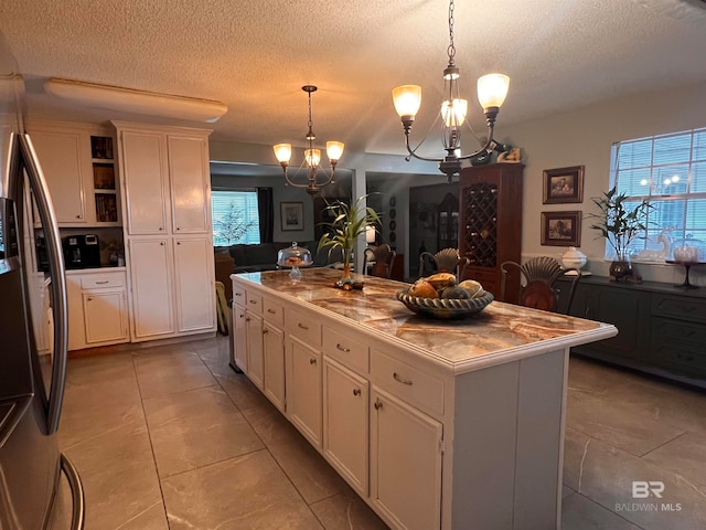 kitchen featuring stainless steel refrigerator with ice dispenser, white cabinets, decorative light fixtures, a center island with sink, and a chandelier