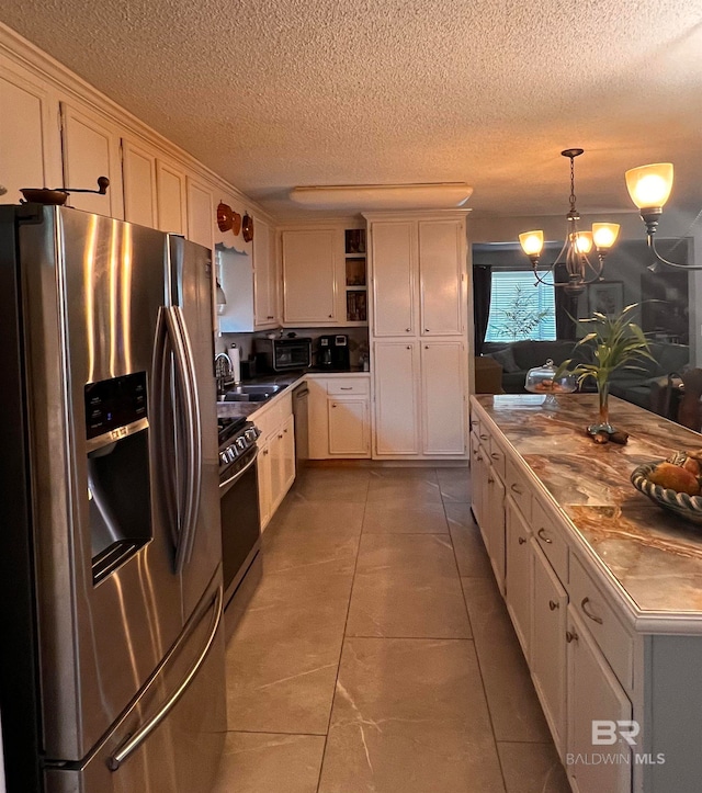 kitchen featuring tile patterned floors, stainless steel appliances, white cabinets, a chandelier, and hanging light fixtures