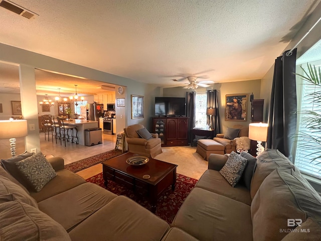 living room with ceiling fan with notable chandelier, light tile patterned flooring, and a textured ceiling