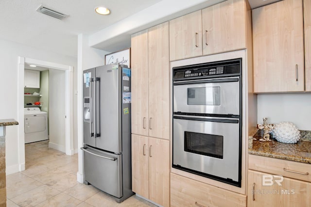 kitchen with appliances with stainless steel finishes, washer / dryer, light brown cabinets, stone countertops, and light tile patterned floors