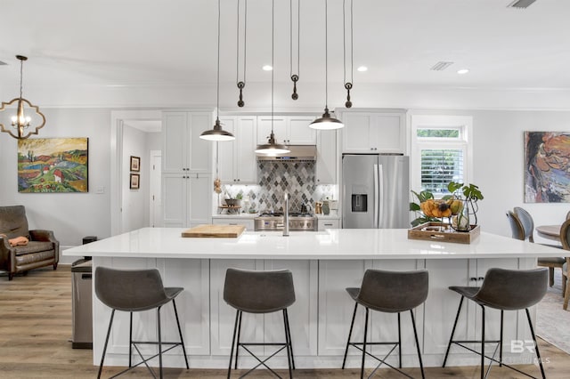 kitchen featuring a spacious island, white cabinetry, hanging light fixtures, stainless steel fridge, and a kitchen breakfast bar