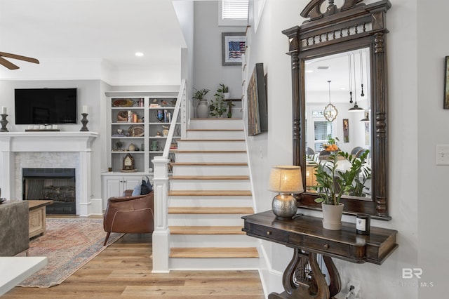 stairs featuring wood-type flooring, ornamental molding, and ceiling fan