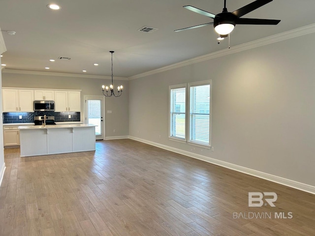 kitchen featuring crown molding, a kitchen island with sink, decorative light fixtures, and light hardwood / wood-style floors