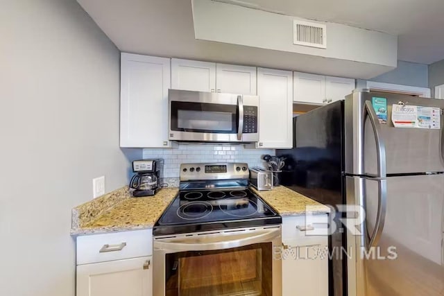 kitchen with white cabinets, appliances with stainless steel finishes, backsplash, and light stone countertops