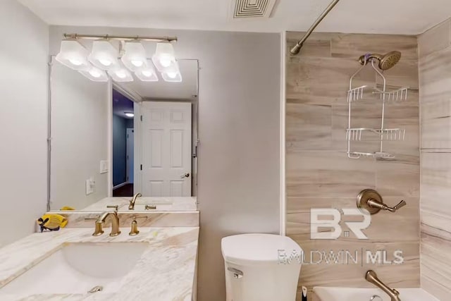 full bathroom featuring tiled shower / bath, vanity, and toilet