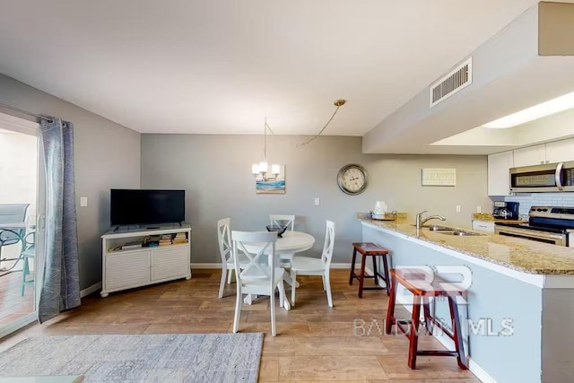 kitchen featuring hanging light fixtures, white cabinets, kitchen peninsula, stainless steel appliances, and sink