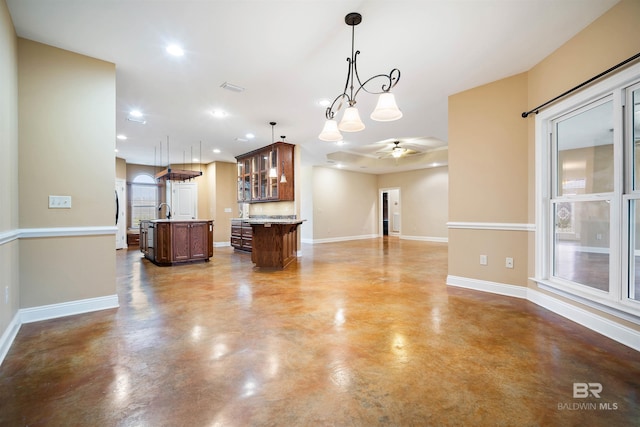 kitchen with sink, a kitchen bar, ceiling fan with notable chandelier, decorative light fixtures, and a kitchen island