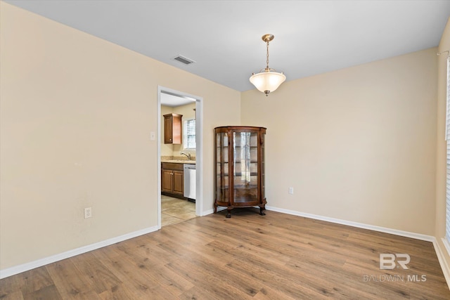 unfurnished room with light wood finished floors, a sink, visible vents, and baseboards