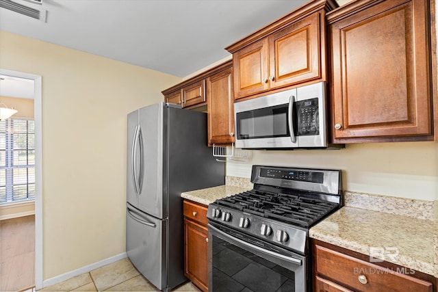 kitchen featuring appliances with stainless steel finishes, light stone countertops, visible vents, and brown cabinets