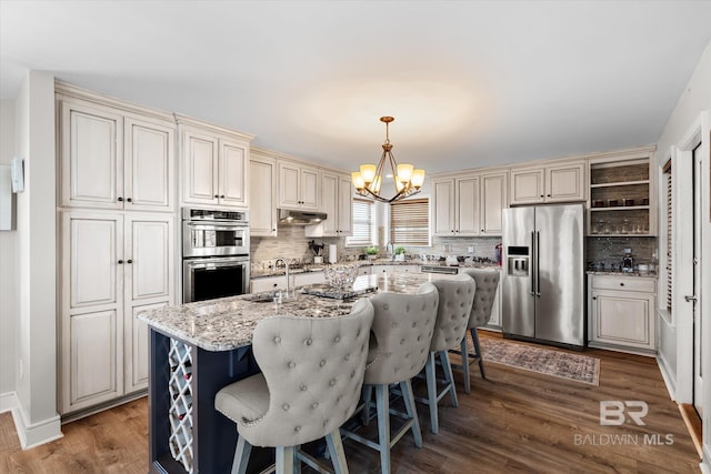 kitchen with stainless steel appliances, light stone countertops, dark hardwood / wood-style flooring, and a center island