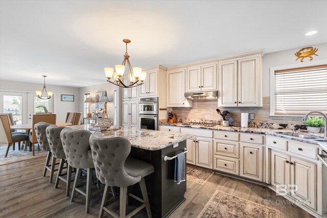 kitchen featuring a kitchen island, a kitchen breakfast bar, stainless steel appliances, hanging light fixtures, and hardwood / wood-style flooring