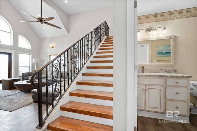 stairs with ceiling fan, hardwood / wood-style flooring, sink, and high vaulted ceiling