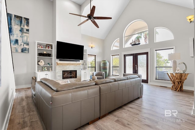 living room with a fireplace, a wealth of natural light, high vaulted ceiling, and light wood-type flooring