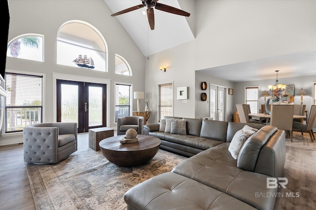 living room with wood-type flooring, ceiling fan with notable chandelier, french doors, and high vaulted ceiling