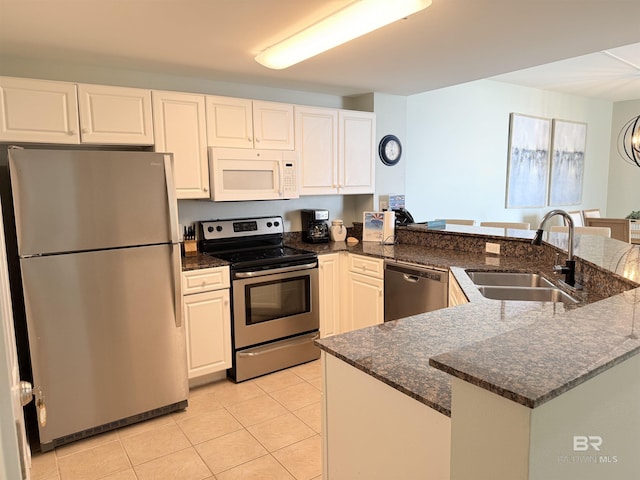 kitchen with dark stone countertops, light tile patterned floors, a sink, appliances with stainless steel finishes, and white cabinetry