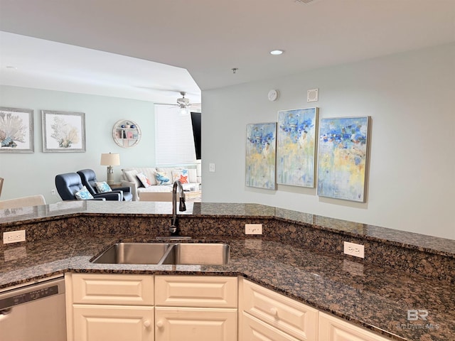 kitchen with a sink, open floor plan, ceiling fan, dark stone counters, and stainless steel dishwasher