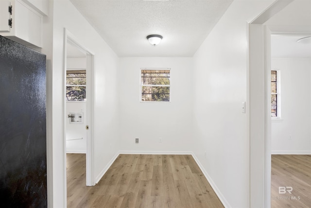 corridor featuring baseboards, light wood-type flooring, and a textured ceiling