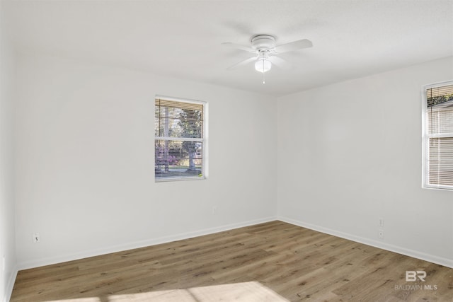 spare room with a ceiling fan, plenty of natural light, wood finished floors, and baseboards