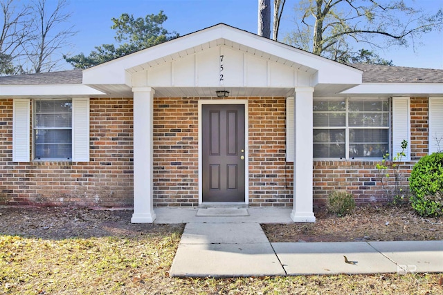 property entrance featuring brick siding and a shingled roof