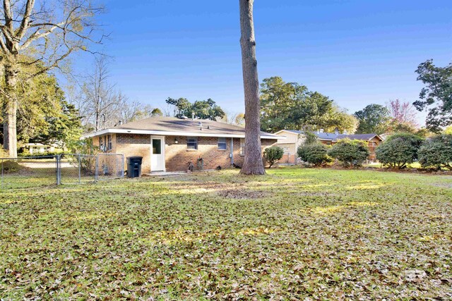 back of house with brick siding, fence, a yard, and a gate