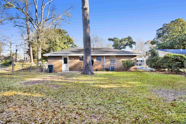 back of property with a lawn, a gate, central AC, fence, and brick siding