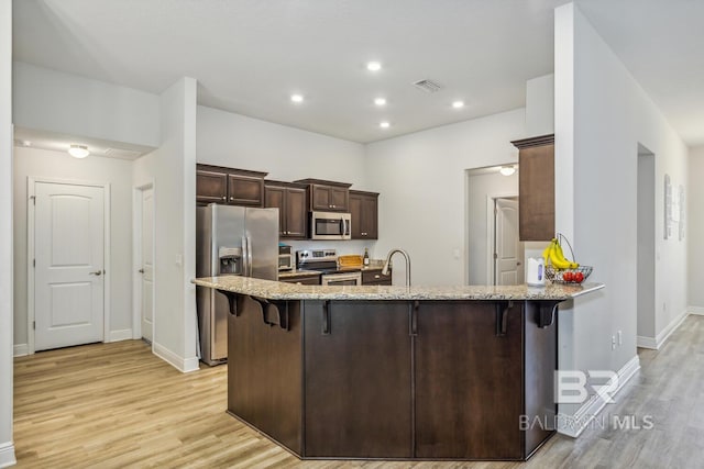 kitchen with a kitchen bar, light hardwood / wood-style floors, appliances with stainless steel finishes, and kitchen peninsula