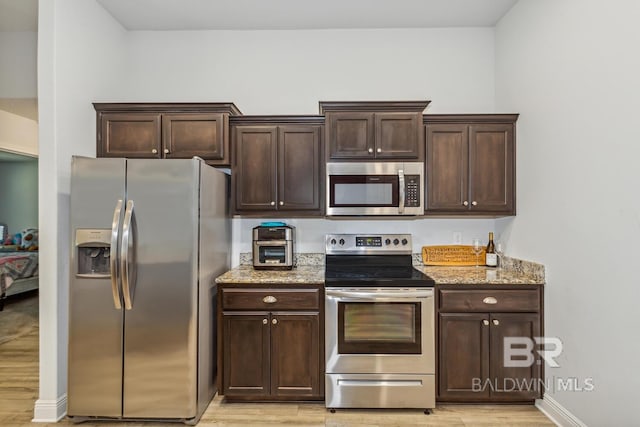 kitchen with dark brown cabinets, light hardwood / wood-style flooring, stainless steel appliances, and light stone counters