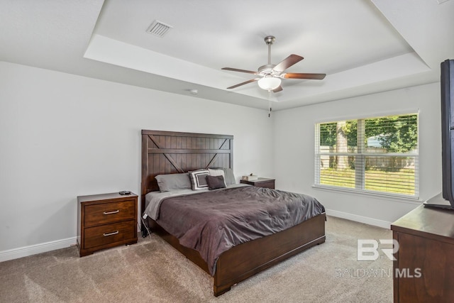 carpeted bedroom with ceiling fan and a raised ceiling