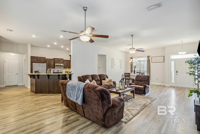 living room featuring ceiling fan with notable chandelier and light hardwood / wood-style flooring