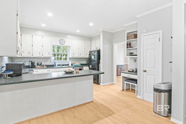 kitchen with light hardwood / wood-style floors, crown molding, kitchen peninsula, black refrigerator, and white cabinetry