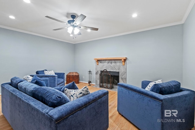 living room featuring ceiling fan, crown molding, hardwood / wood-style floors, and a tiled fireplace