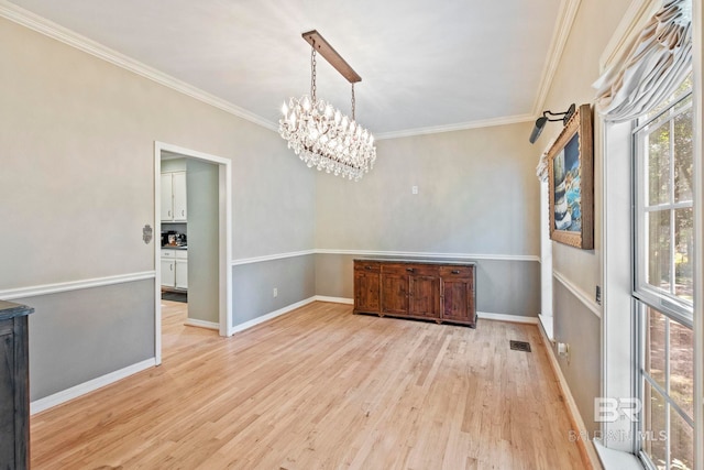 unfurnished dining area featuring an inviting chandelier, ornamental molding, and light hardwood / wood-style flooring