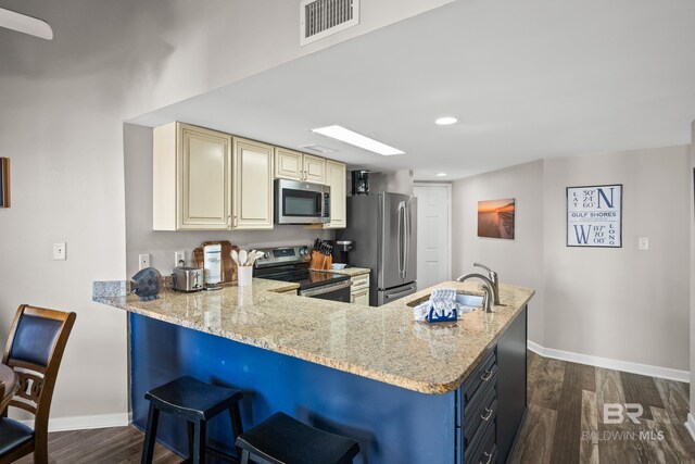 kitchen with dark wood-style flooring, a sink, appliances with stainless steel finishes, cream cabinetry, and light stone countertops