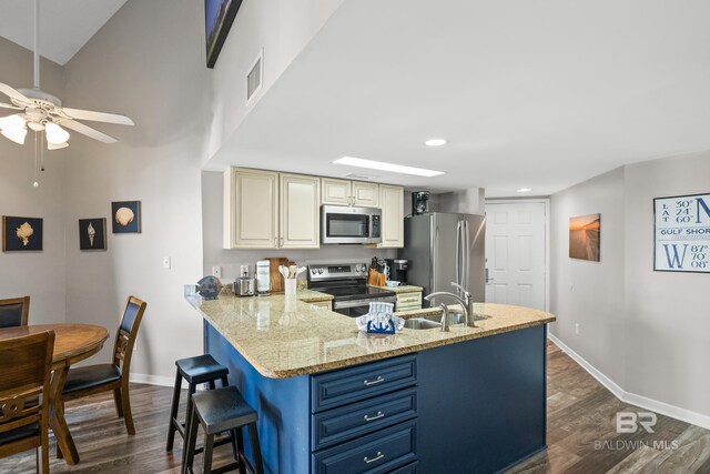 kitchen with cream cabinets, stainless steel appliances, a sink, baseboards, and dark wood finished floors