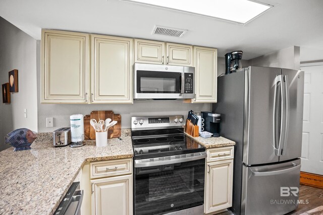 kitchen featuring appliances with stainless steel finishes, cream cabinets, visible vents, and light stone countertops